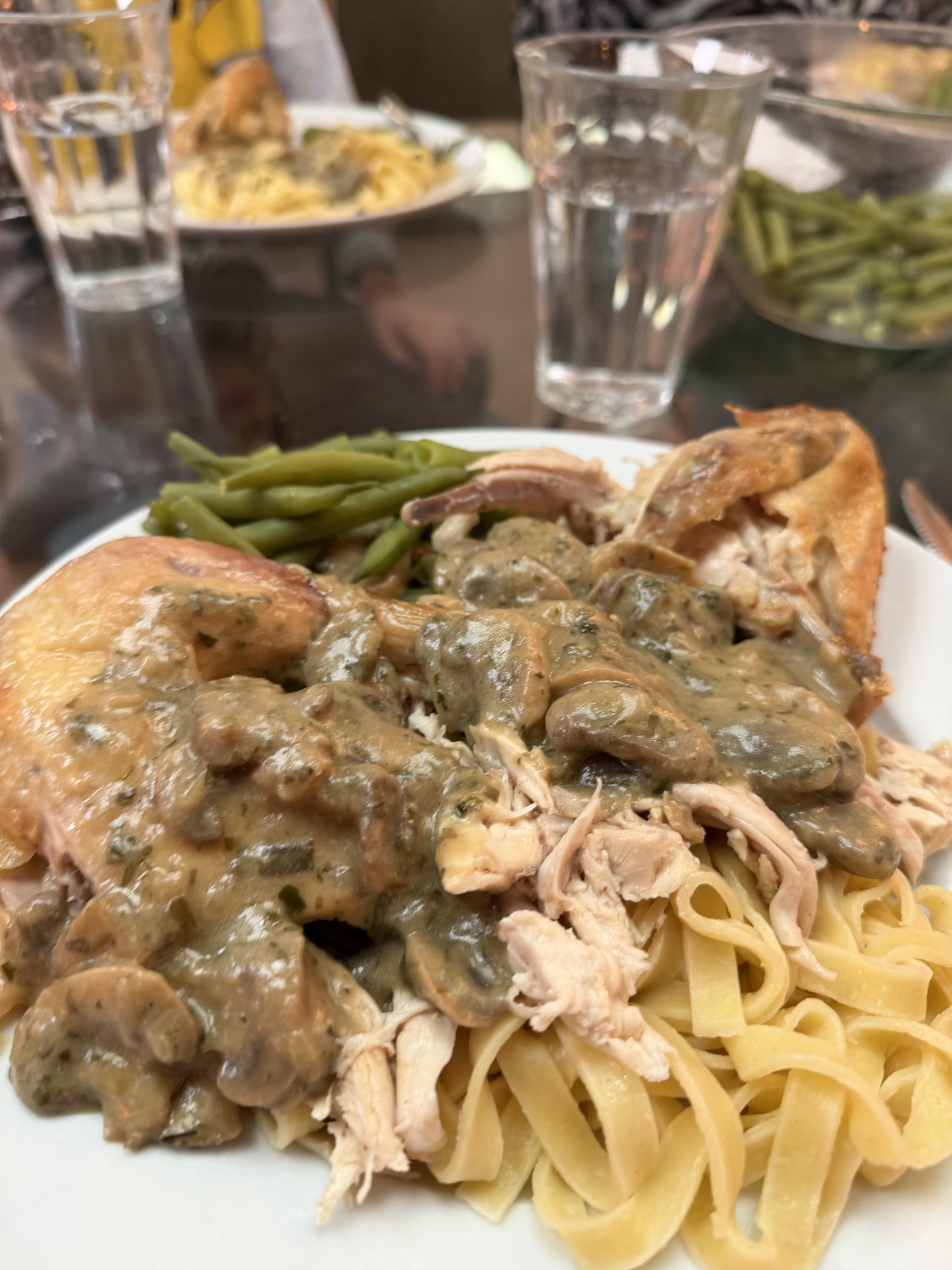 This photo captures a delicious home-cooked meal featuring chicken with a rich mushroom sauce, accompanied by egg noodles and green beans, served on a dining table